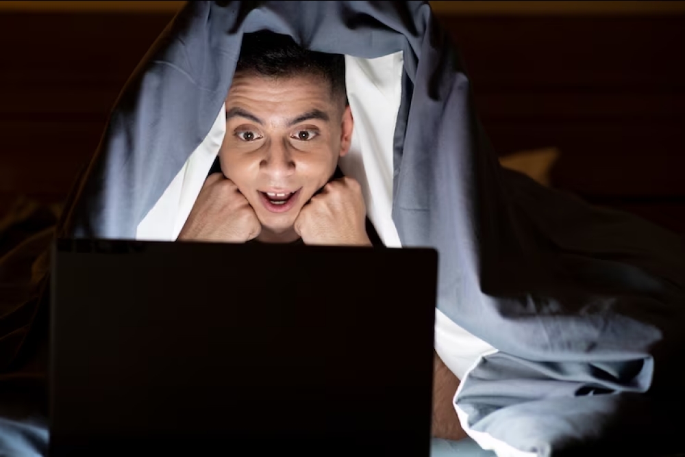 Seorang pria sedang menonton laptop dengan balutan kasur